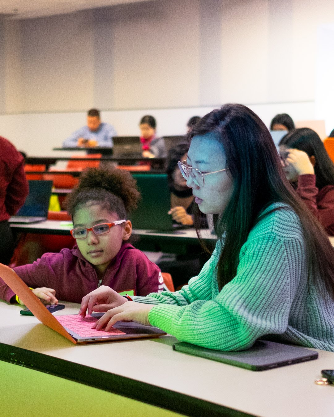 Two young women work at a desk on a laptop.